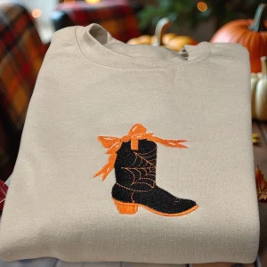 Embroidered spooky cowboy boot with cobweb and bow sweatshirt or hoodie. Western Halloween clothing.